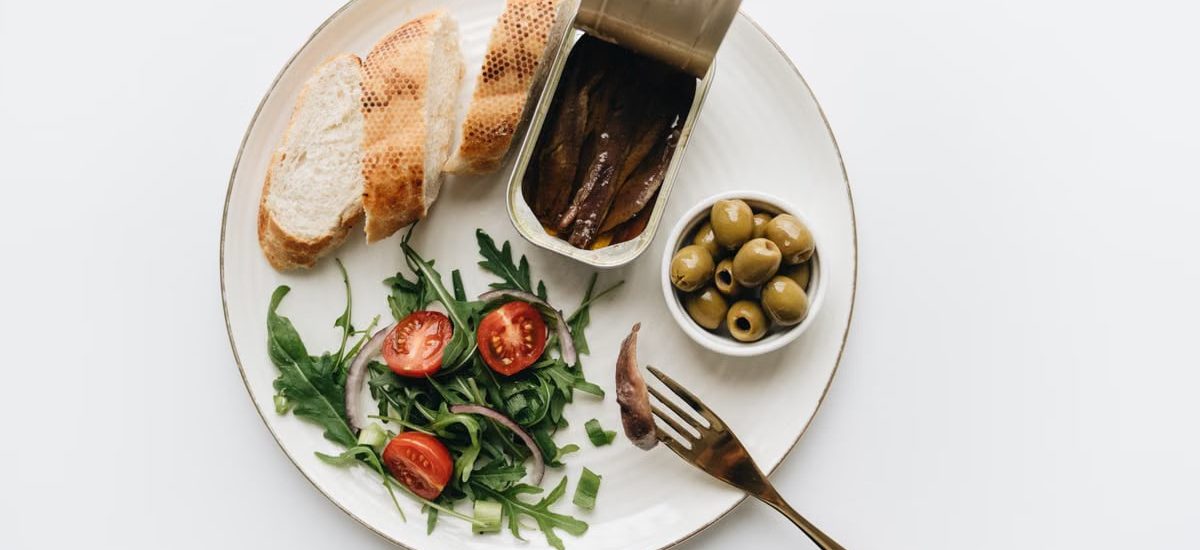A gourmet Mediterranean dish featuring anchovies, olives, bread, and fresh salad on a plate.