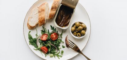A gourmet Mediterranean dish featuring anchovies, olives, bread, and fresh salad on a plate.