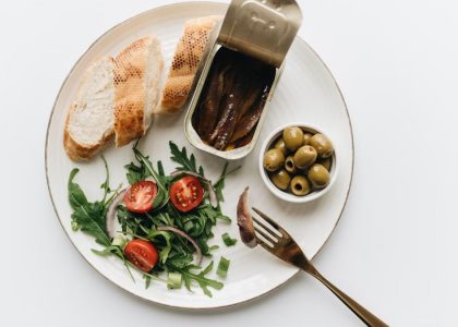 A gourmet Mediterranean dish featuring anchovies, olives, bread, and fresh salad on a plate.