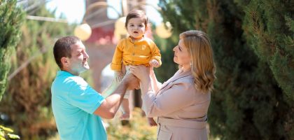 A joyful family moment with parents lifting their happy baby in an outdoor park setting.