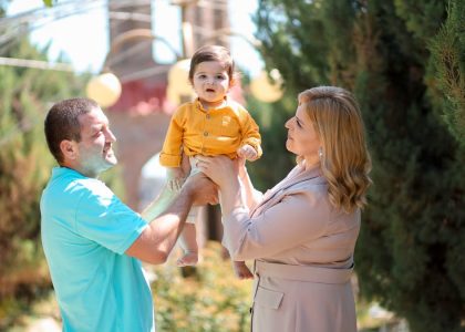 A joyful family moment with parents lifting their happy baby in an outdoor park setting.